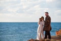 Happy handsome young pair trendy bearded man and woman in autumn coat looking through binoculars near sea shore during sunset with