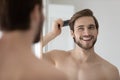 Happy handsome young shirtless man combing smooth straight hair