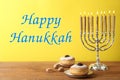 Happy Hanukkah. Silver menorah, dreidels and sufganiyot on wooden table against yellow background Royalty Free Stock Photo