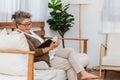 Happy & healthly retired smiling senior woman or pensioner reading book resting or sitting on couch or sofa at home. Eldery adult Royalty Free Stock Photo