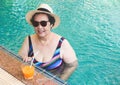 Happy and healthy Asian senior  woman wearing colorful swiming suit,  straw hat and sunglasses  drinking  orange juice  in the Royalty Free Stock Photo