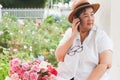 Happy and healthy Asian senior woman wearing hat  sitting by roses bucket in rose garden talking on mobile phone.Senior people Royalty Free Stock Photo