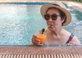 Happy and healthy Asian senior  woman wearing straw hat and sunglasses,  drinking  orange juice  in the swimming pool, smiling and Royalty Free Stock Photo