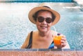Happy and healthy Asian senior  woman wearing straw hat and sunglasses,  drinking  orange juice  in the swimming pool, smiling Royalty Free Stock Photo