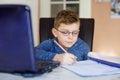 Happy healthy kid boy with glasses making school homework at home with notebook. Interested child writing essay with Royalty Free Stock Photo