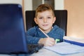 Happy healthy kid boy with glasses making school homework at home with notebook. Interested child writing essay with Royalty Free Stock Photo