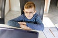 Happy healthy kid boy with glasses making school homework at home with notebook. Interested child writing essay with Royalty Free Stock Photo