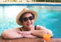 Happy and healthy senior Asian woman wearing straw hat and sunglasses  drinking  orange juice  in the swimming pool smiling and Royalty Free Stock Photo
