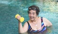 Happy and healthy senior Asian woman  working out in the pool with yellow dumbbells, smiling and looking at camera. Elderly sports Royalty Free Stock Photo