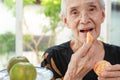 Happy healthy senior woman eating tangerine deliciously,asian old elderly opening her mouth wide to taste delicious organic orange Royalty Free Stock Photo