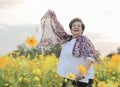 Happy and healthy senior woman standing in yellow cosmos flower garden open her arms with scarf happily