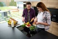 Happy heterosexual couple of handsome man and his pregnant wife preparing delicious healthy raw salad in kitchen island, enjoying Royalty Free Stock Photo