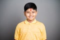 Happy Hindu kid with kumkum Bindi or Tilak on forehead by looking at camera on studio background - concept of smiling and positive