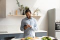 Happy Black chef man using mobile phone in home kitchen Royalty Free Stock Photo