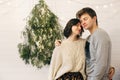 Happy hipster couple gently hugging at modern christmas tree lights in stylish festive room. Celebrating Christmas or New Year`s Royalty Free Stock Photo