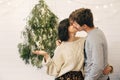 Happy hipster couple having fun and kissing at modern christmas tree lights in stylish festive room. Celebrating Christmas or New Royalty Free Stock Photo