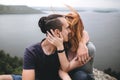 Happy hipster couple kissing on top of rock mountain with beautiful view on river. Tourist couple sitting and hugging on windy Royalty Free Stock Photo