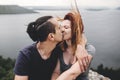 Happy hipster couple kissing on top of rock mountain with beautiful view on river. Tourist couple sitting and hugging on windy Royalty Free Stock Photo