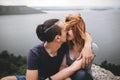 Happy hipster couple kissing on top of rock mountain with beautiful view on river. Tourist couple sitting and hugging on windy Royalty Free Stock Photo