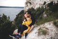 Happy hipster couple kissing on top of rock mountain with beautiful view on river. Tourist couple sitting and hugging on windy Royalty Free Stock Photo