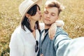 Happy hipster couple making selfie in sunny wildflower meadow, traveling in mountains. Stylish young family smiling and enjoying Royalty Free Stock Photo