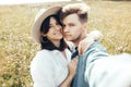 Happy hipster couple making selfie in sunny wildflower meadow, traveling in mountains. Stylish young family smiling and enjoying Royalty Free Stock Photo