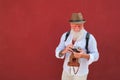 Happy hipster man using old vintage camera standing on red wall - Mature stylish photographer having fun traveling the world -