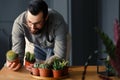 Happy hipster whose hobby is gardening looking at cacti at wooden table