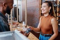 Happy hispanic customer paying for a meal in a restaurant using a nfc machine and credit card. Smiling young woman Royalty Free Stock Photo