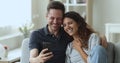 Happy spouses relaxing at home watching funny videos on cellphone