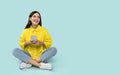 Happy hispanic young woman in casual clothes sitting on floor, using cell phone isolated on blue studio background Royalty Free Stock Photo