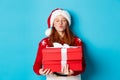 Happy holidays and Christmas concept. Cute redhead girl holding presents and pucker lips for kiss, wearing santa hat and Royalty Free Stock Photo