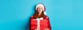 Happy holidays and Christmas concept. Cute redhead girl holding presents and pucker lips for kiss, wearing santa hat and Royalty Free Stock Photo