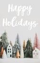 Happy holidays Greeting card. Happy holidays text handwritten on christmas little houses and trees on white background,  winter Royalty Free Stock Photo