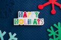 Happy Holidays plaque message and colorful wooden snowflakes on blue background, for Christmas projects Royalty Free Stock Photo