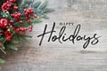 Happy Holidays Text with Christmas Evergreen Branches and Red Winter Holiday Berries in Corner Over Rustic Wooden Background