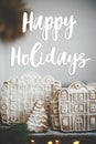 Happy Holidays text on christmas gingerbread cookie houses and trees with golden lights on rustic table. Season`s greetings card. Royalty Free Stock Photo