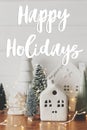 Happy Holidays text on festive christmas scene, miniature holiday village. Stylish Christmas trees and little houses. Season`s Royalty Free Stock Photo