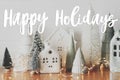 Happy Holidays text on festive Christmas scene, miniature holiday village. Stylish Christmas trees and little houses. Season`s Royalty Free Stock Photo