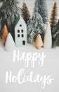 Happy holidays text handwritten on christmas little houses and trees on white background,  winter holiday village scene. Greeting Royalty Free Stock Photo