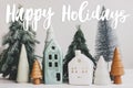 Happy holidays text handwritten on little houses and christmas trees, miniature winter village scene. Greeting card, modern Royalty Free Stock Photo