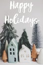 Happy holidays text handwritten on little houses and christmas trees, miniature winter village scene. Greeting card, modern Royalty Free Stock Photo