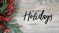 Happy Holidays Text with Holiday Evergreen Branches and Red Berries Over Rustic Wood Background Royalty Free Stock Photo