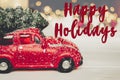 Happy holidays text, seasonal greetings card sign. red car toy w Royalty Free Stock Photo