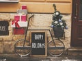 Happy Holidays text sign on board and stylish bicycle with christmas gifts and modern christmas tree at store front at holiday Royalty Free Stock Photo