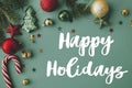 Happy Holidays text sign on christmas festive decorations, confetti, fir branches on green background flat lay. Season`s greeting Royalty Free Stock Photo