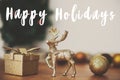 Happy Holidays text sign on golden reindeer, gift box and glitter bauble toys on background of christmas tree with lights on Royalty Free Stock Photo