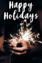 happy holidays text sign, greeting card. happy new year and merry christmas concept. female hand holding a burning sparkler Royalty Free Stock Photo