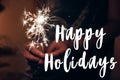 happy holidays text sign, greeting card. happy new year and merry christmas concept. female hand holding a burning sparkler Royalty Free Stock Photo
