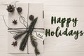 happy holidays text sign, greeting card. stylish christmas rustic gift box flat lay. white present with green tree fir branch and